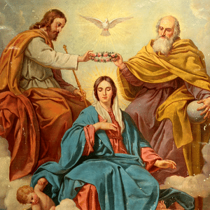 Nossa Senhora ao centro com seu manto azul. Ao seu lado direito Jesus e ao lado esquerdo Deus Pai, ambos segurando uma coroa sobre sua cabeça. Acima da coroa uma pomba representando o Espírito Santo. Tudo isso no céu